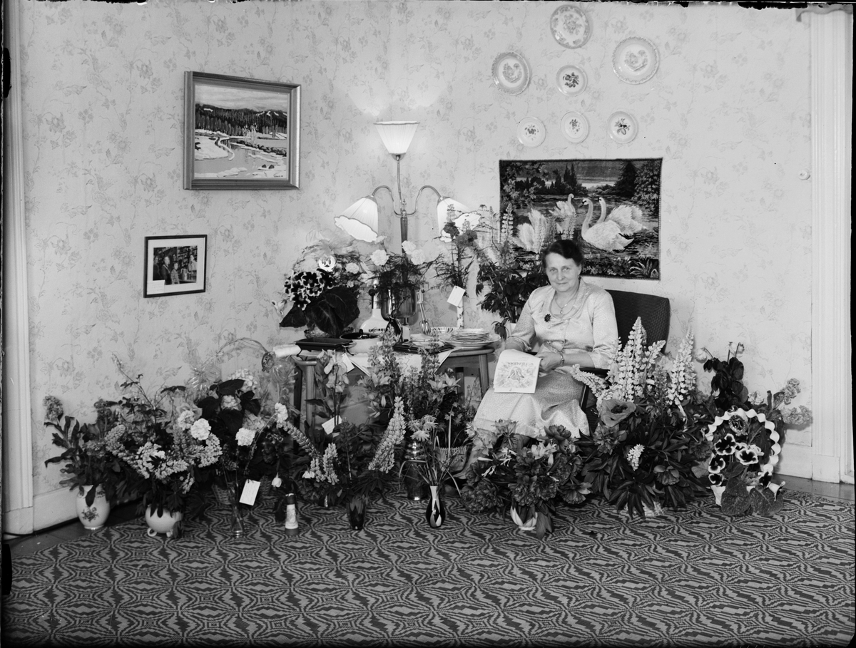 Skötsner-Edhlund, Kvinna i hemmiljö omgiven av blommor, Östhammar, Uppland