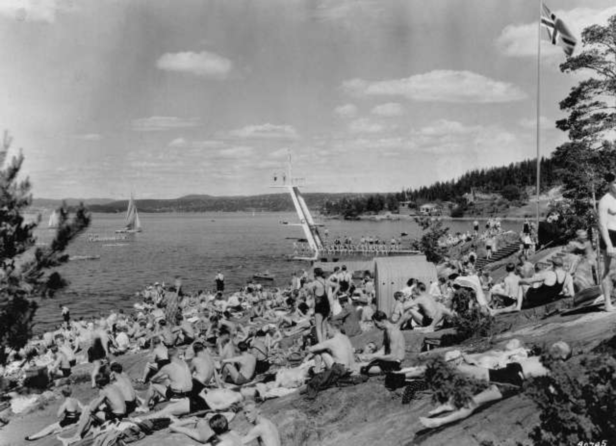 Anders Beer Wilse, Strandliv med badegjester som soler seg på svaberget ved sjøen på Ingierstrand bad utenfor Oslo. Stupetårn i bakgrunnen.