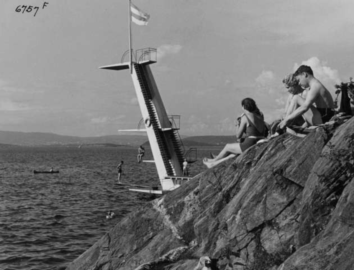 Anders Beer Wilse, Strandliv med badegjester som soler seg på svaberget ved sjøen på Ingierstrand bad utenfor Oslo. Stupetårn i bakgrunnen.