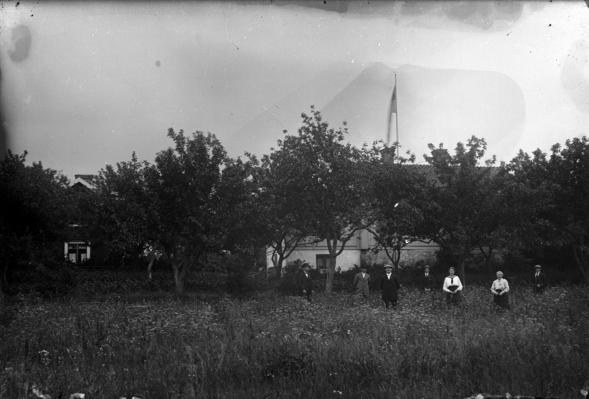 Ester Pettersson, Familjegrupp sju personer i trädgården. Bostadshus i bakgrunden. Bilden tagen i Öskevik.