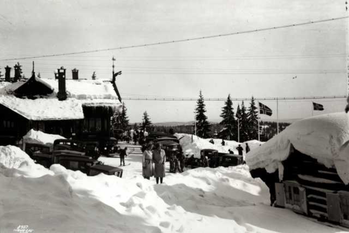 Hermann Christian Neupert, Frognerseteren Restaurant, Nordmarka, Oslo. Vintermotiv. Biler og mennesker foran restauranten. Flaggstenger med flagg.