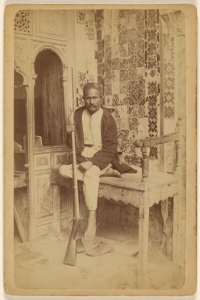 Unknown, [Arab male seated, holding a rifle, with shoes off]