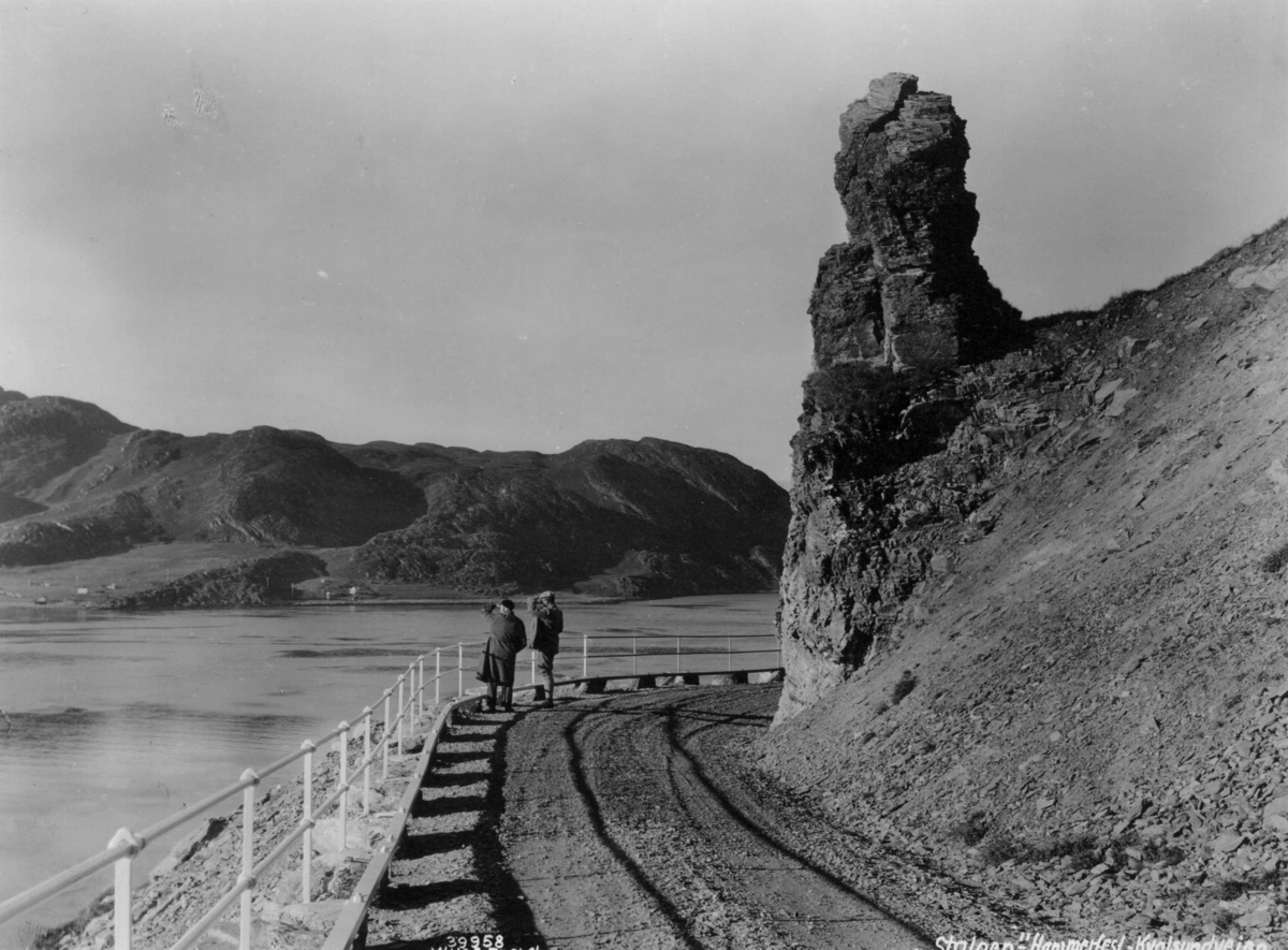 Anders Beer Wilse, Stalloen, en seidestein, ved Kvslsundveien i 1933. To personer på veien ser utover fjorden.