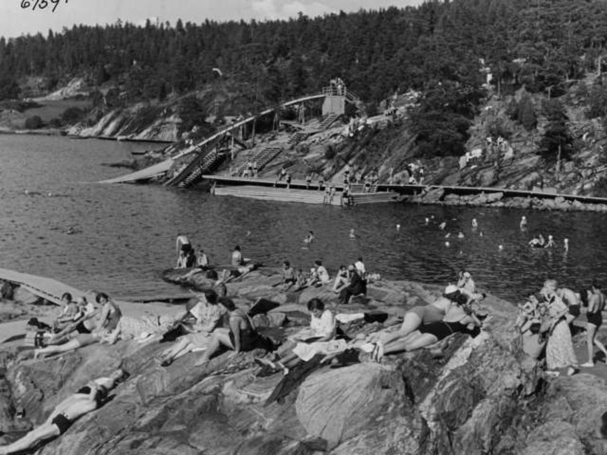 Anders Beer Wilse, Strandliv med badegjester som soler seg på svaberget ved sjøen på Ingierstrand bad utenfor Oslo. Vannsklie i bakgrunnen.