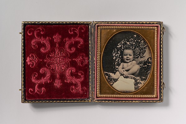 Unknown, [Smiling, Nude Baby Holding Foot, Seated on Furniture Draped with Floral Print Fabric]