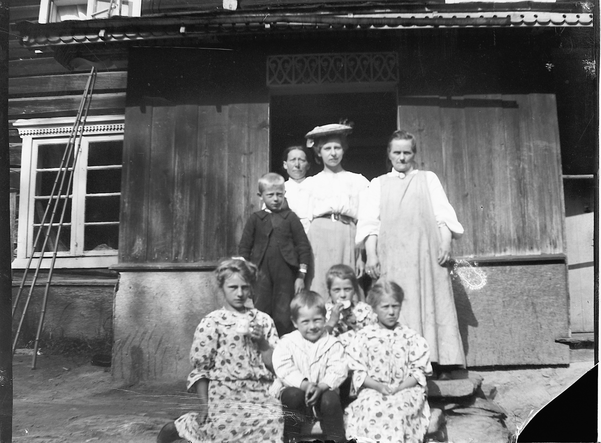 Johs. (Johannes) Johannessen, Gruppe barn og tre kvinner foran inngangen til et hus.