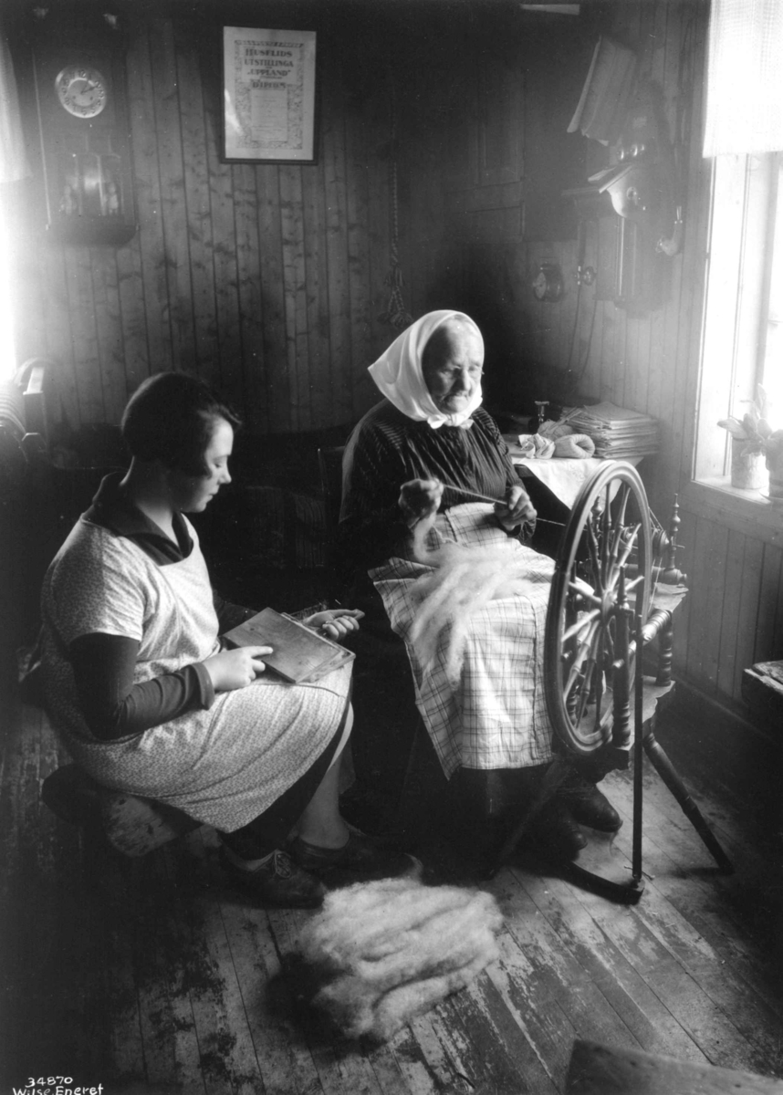 Anders Beer Wilse, To kvinner sitter i en stue og karder og spinner, 1929.