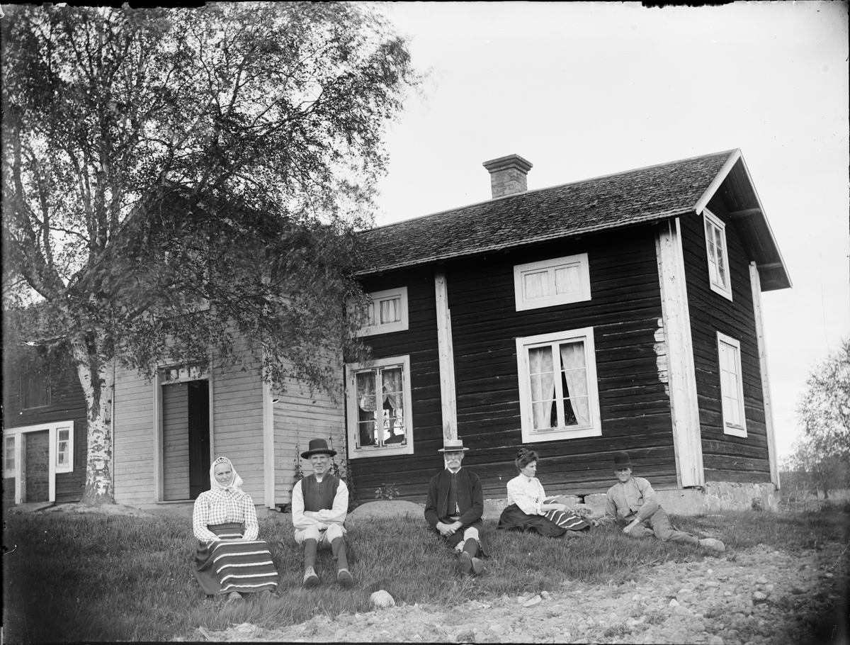 Skötsner-Edhlund, Men and women in folk costume, sitting in the grass in front of residential buildings, Dalarna