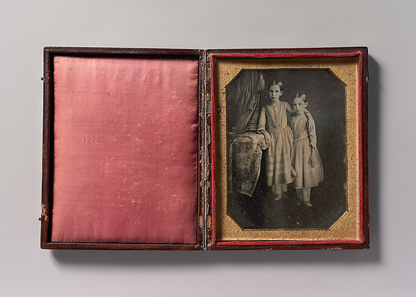 Unknown, [Two Identically Dressed Young Girls Standing Next to a Table]