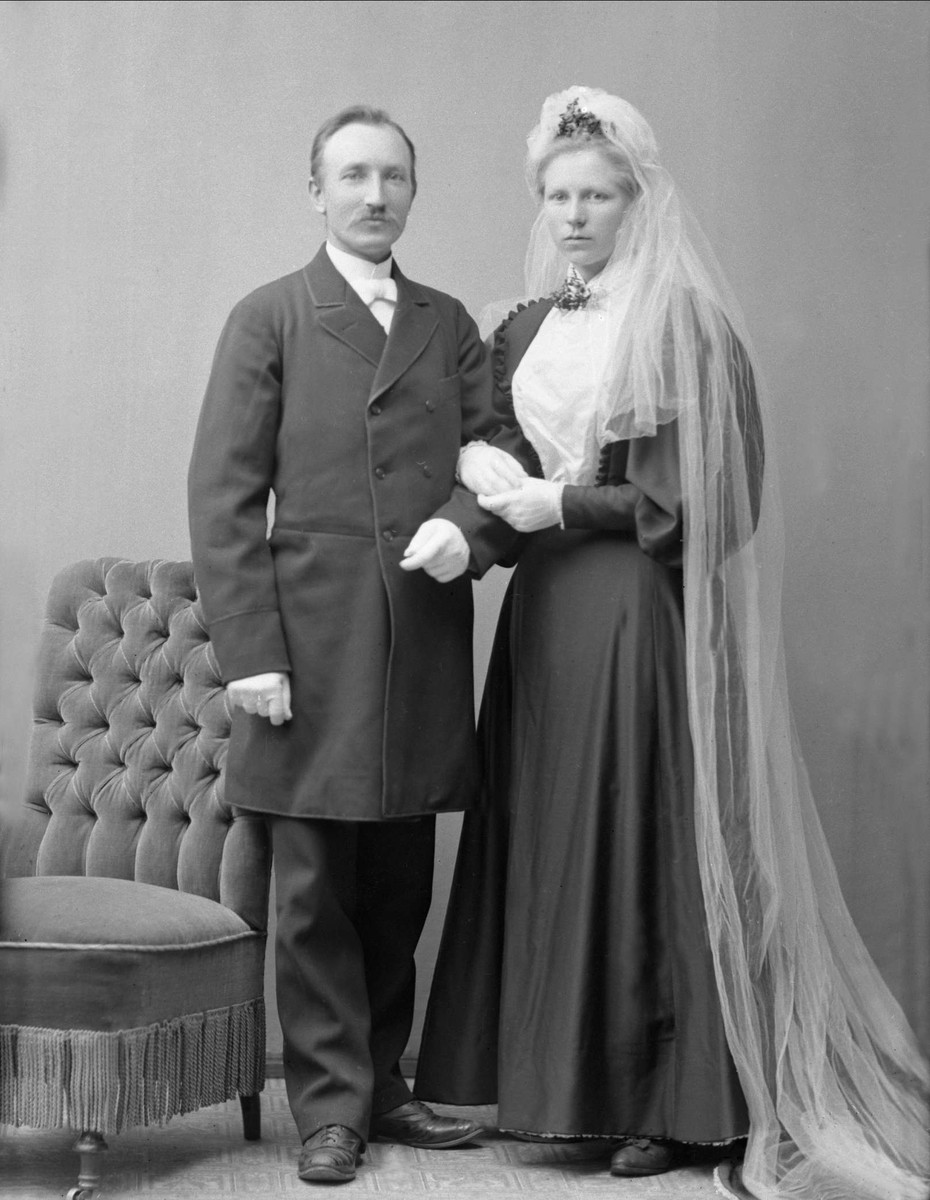 Gustav Borgen, Gruppeportrett, brudepar. Bryllupsbilde, hun i svart kjole og hvitt slør.