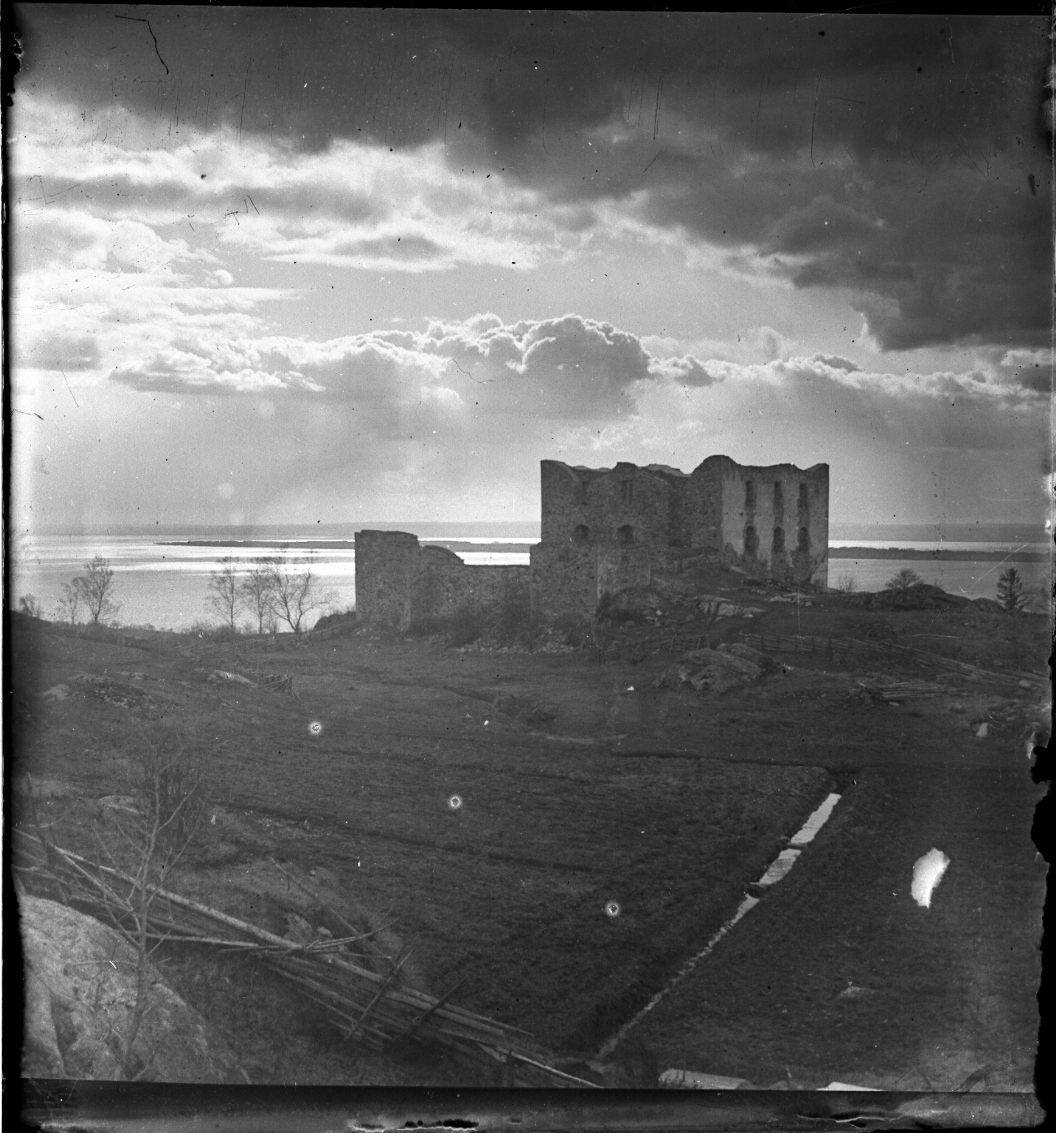 Unknown artist, Fotografi av Brahehus slottsruin mot en mulen himmel över Vättern.