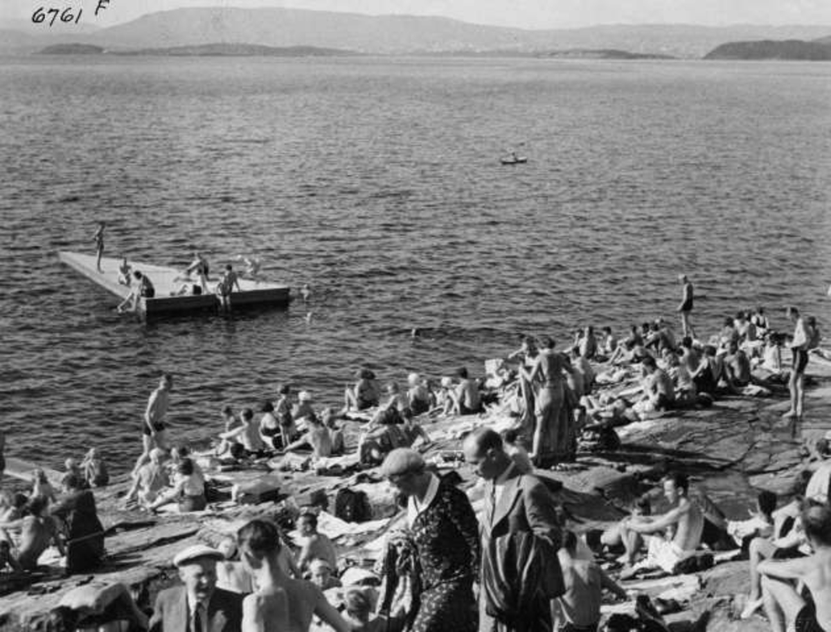Anders Beer Wilse, Strandliv med badegjester som soler seg på svaberget ved sjøen på Ingierstrand bad utenfor Oslo. Flytebrygge i bakgrunnen.