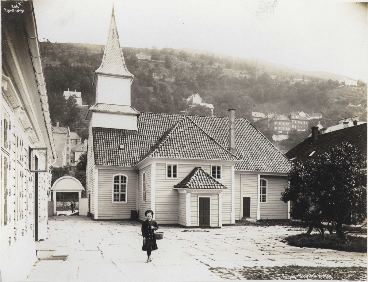 Anders Beer Wilse, St. Jørgens Hospitals kirke, Bergen, Hordaland. Fotografert 1912. Jente med kurv på plassen foran kirken.